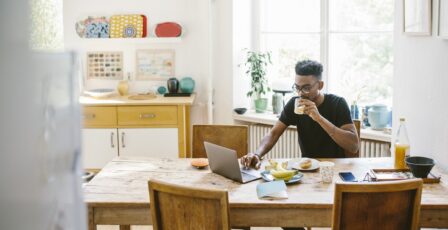 Young man drinking juice while using laptop at table in house