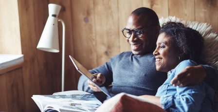 Couple in room with wooden walls cuddling up on sofa with tablet