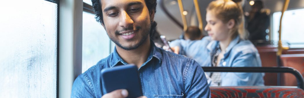 Man smiling while engaging with his phone in the bus