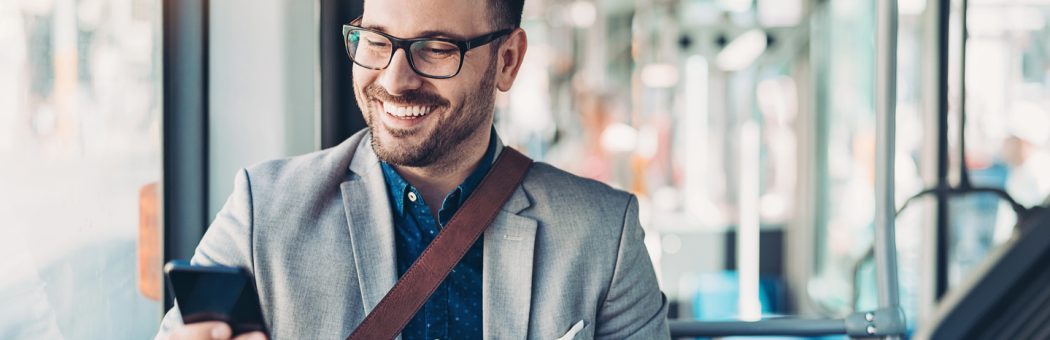 Man smiling while using his phone on a bus