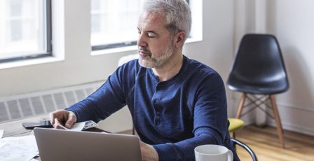 Man looking at papers while sat with a laptop