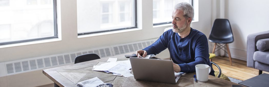Man using a laptop whilst looking at paperwork