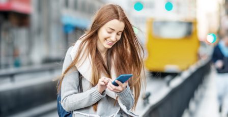 Girl checking her mobile phone with a bus in the background