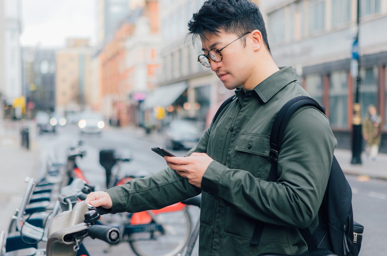 Young man using phone on the street with rental bike