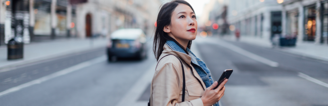 Woman in street booking a taxi using her phone