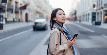 Woman in street booking a taxi using her phone