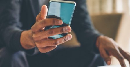 Man looking at his phone while using a laptop