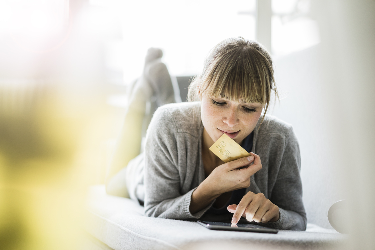 Woman lying on couch with credit card and tablet