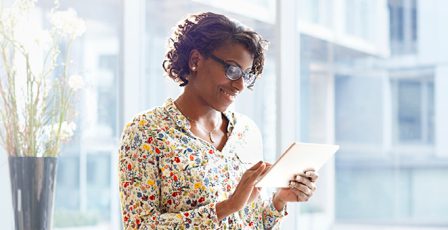 Smiling businessperson standing by a window looking at a tablet