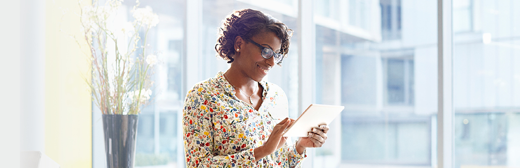 Smiling businessperson standing by a window looking at a tablet