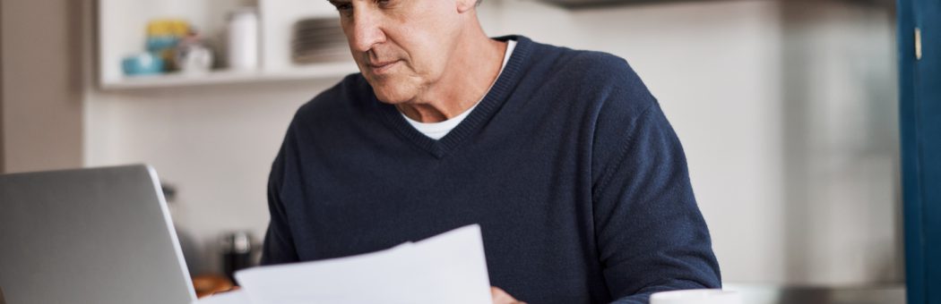 Mature man checking paperwork on his computer