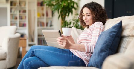 A woman sits on her sofa streaming on her digital tablet