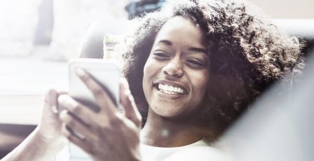 Woman smiling while using her phone on the sofa