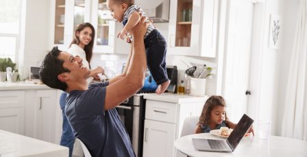 Young Hispanic family in their kitchen, dad lifting baby in the air