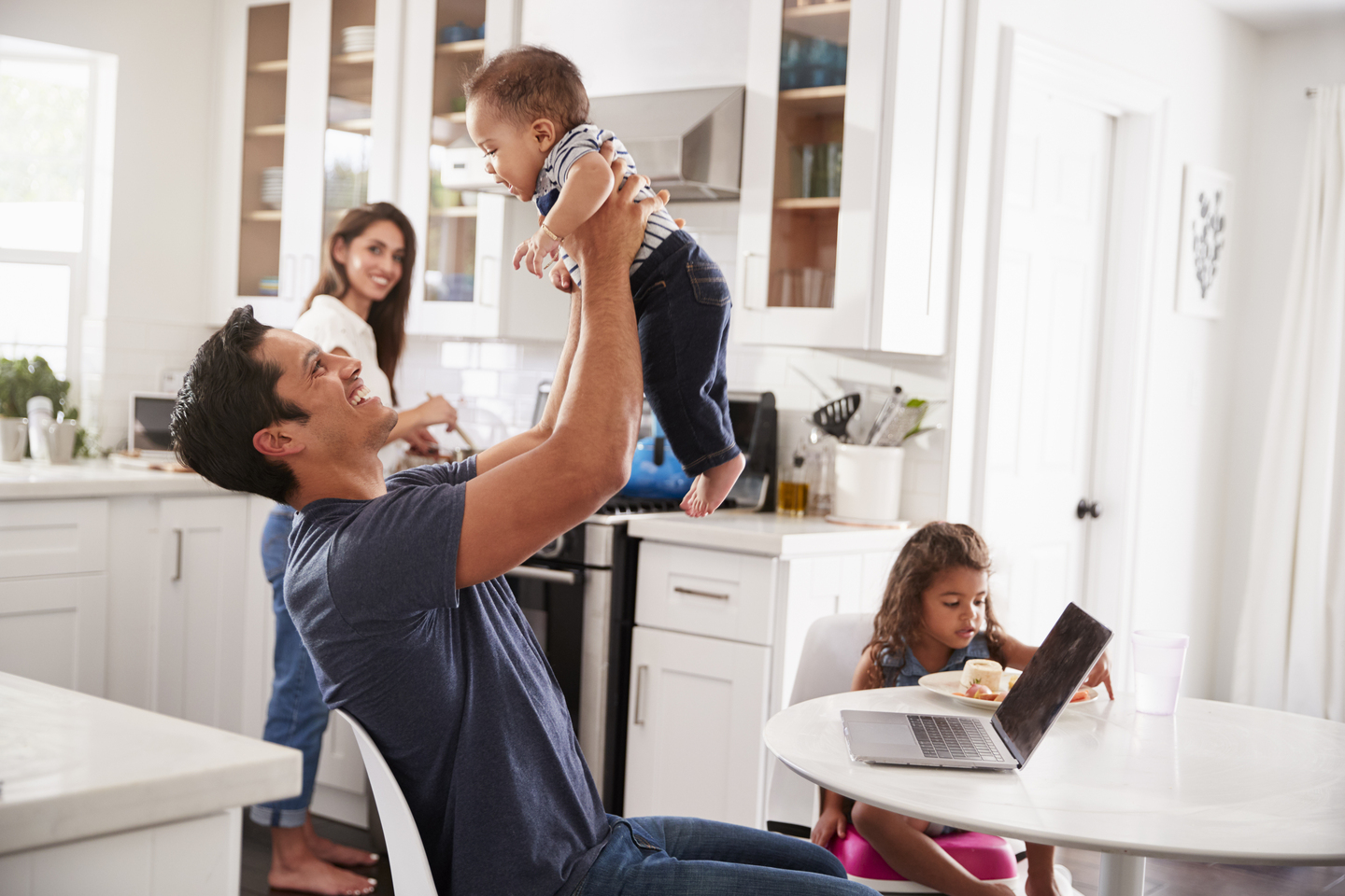 Young Hispanic family in their kitchen, dad lifting baby in the air