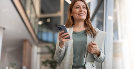 smiling woman holding phone whilst standing up