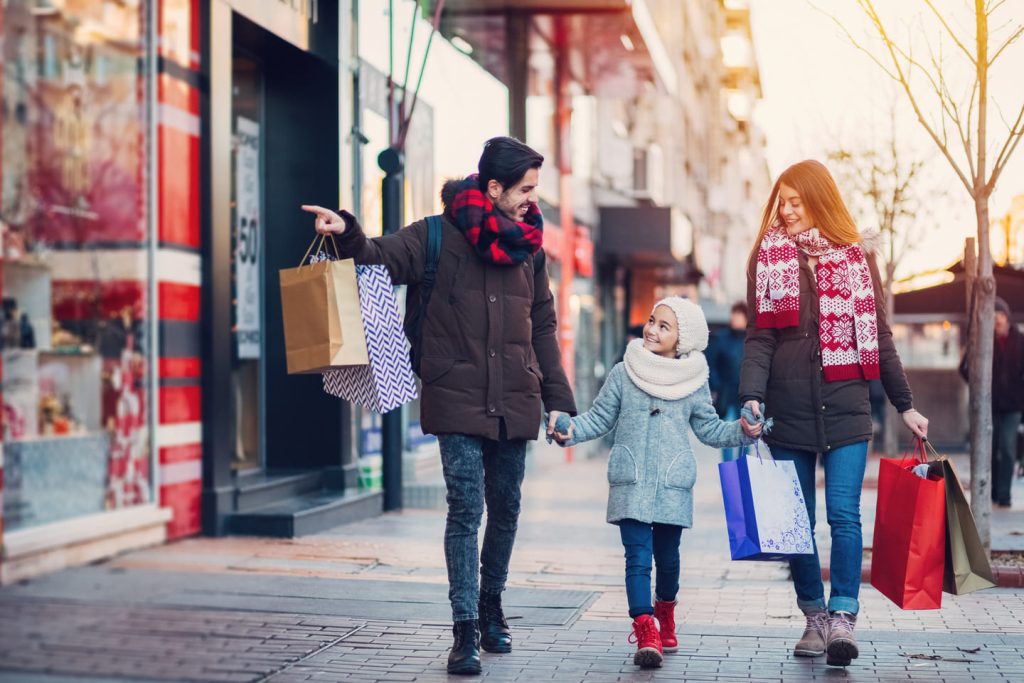 A couple and young child carrying shopping bags through a highstreet during winter