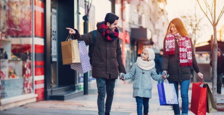 A couple and young child carrying shopping bags through a highstreet during winter