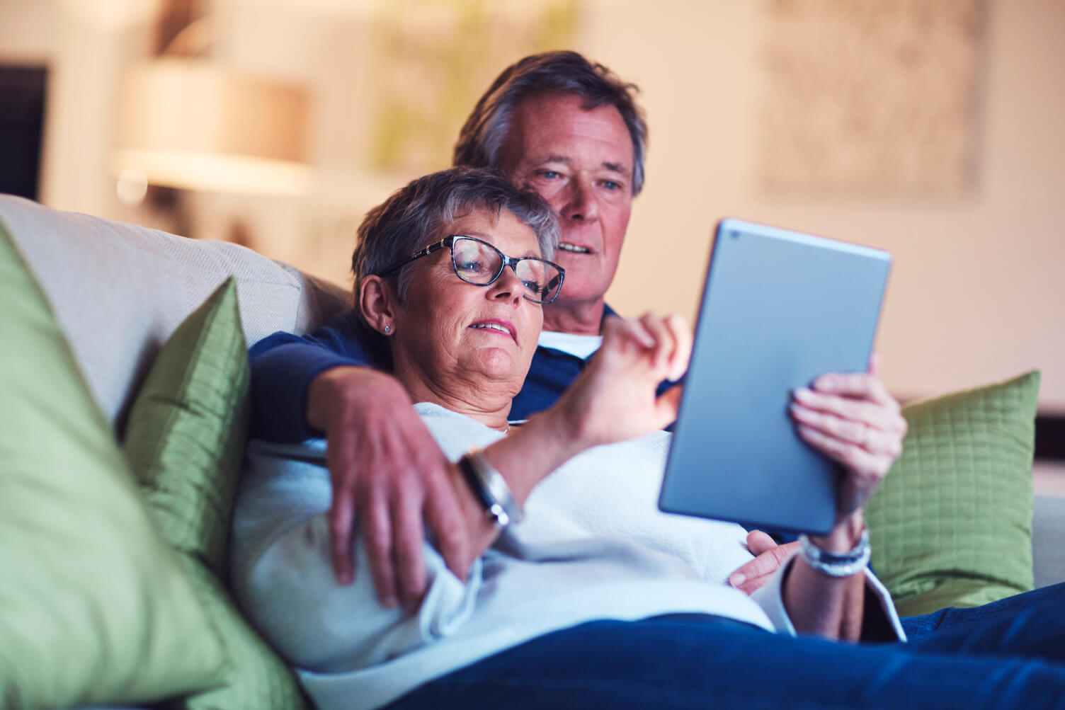 Older couple relaxing on the sofa while browsing on a tablet