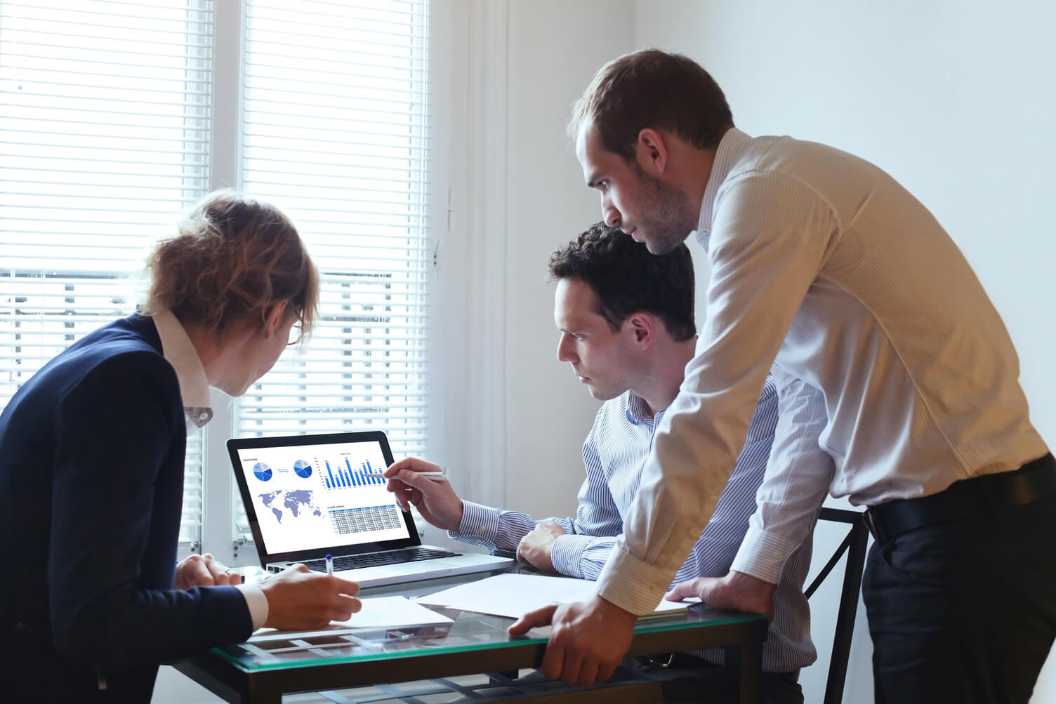 a woman and two men looking at data on a laptop screen