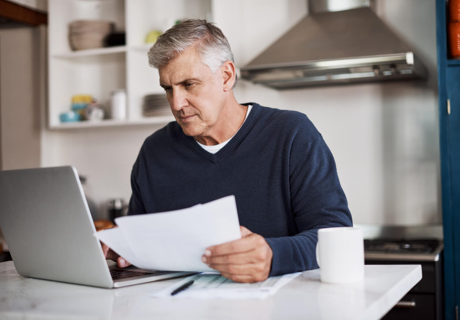 Mature man checking paperwork with a laptop