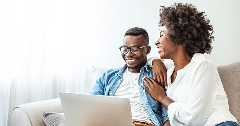 A couple smiling while browsing on a laptop