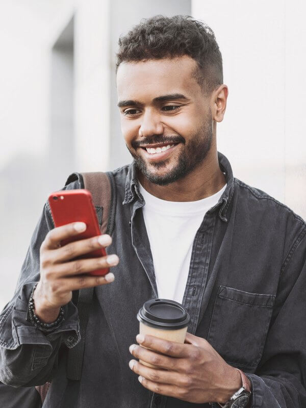 Young man smiling at a mobile phone while holding a takeaway drinks cup