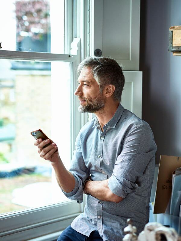 Man looking out the window with his mobile phone