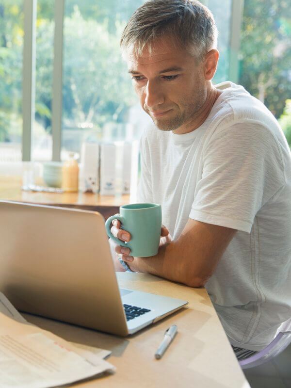 Mature man looking at his laptop while holding a hot drink