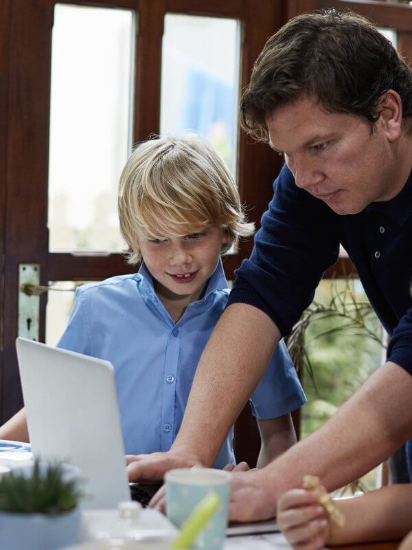 Man assisting a child with school work on a laptop