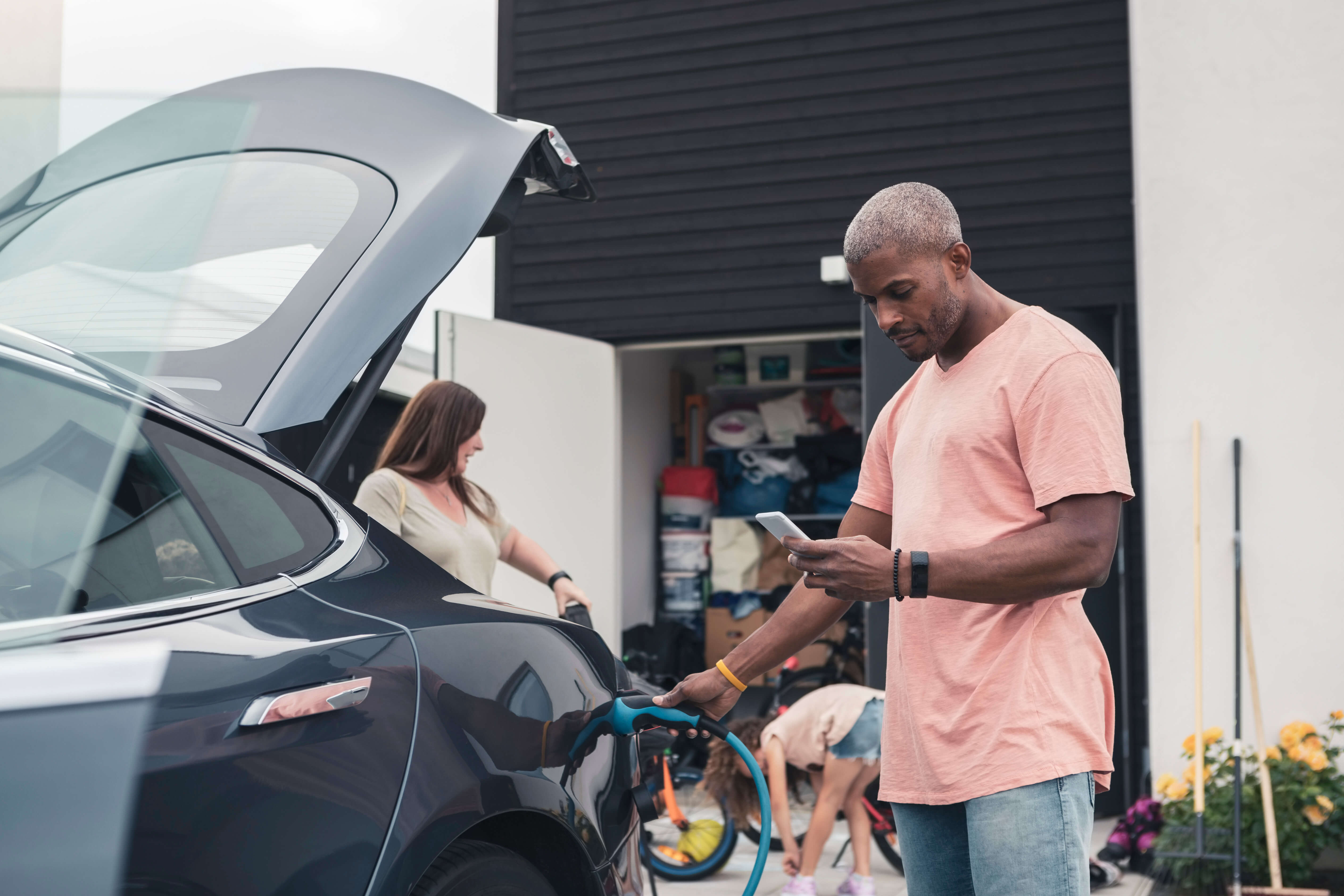 A family in a driveway with a charger plugged into an electric car