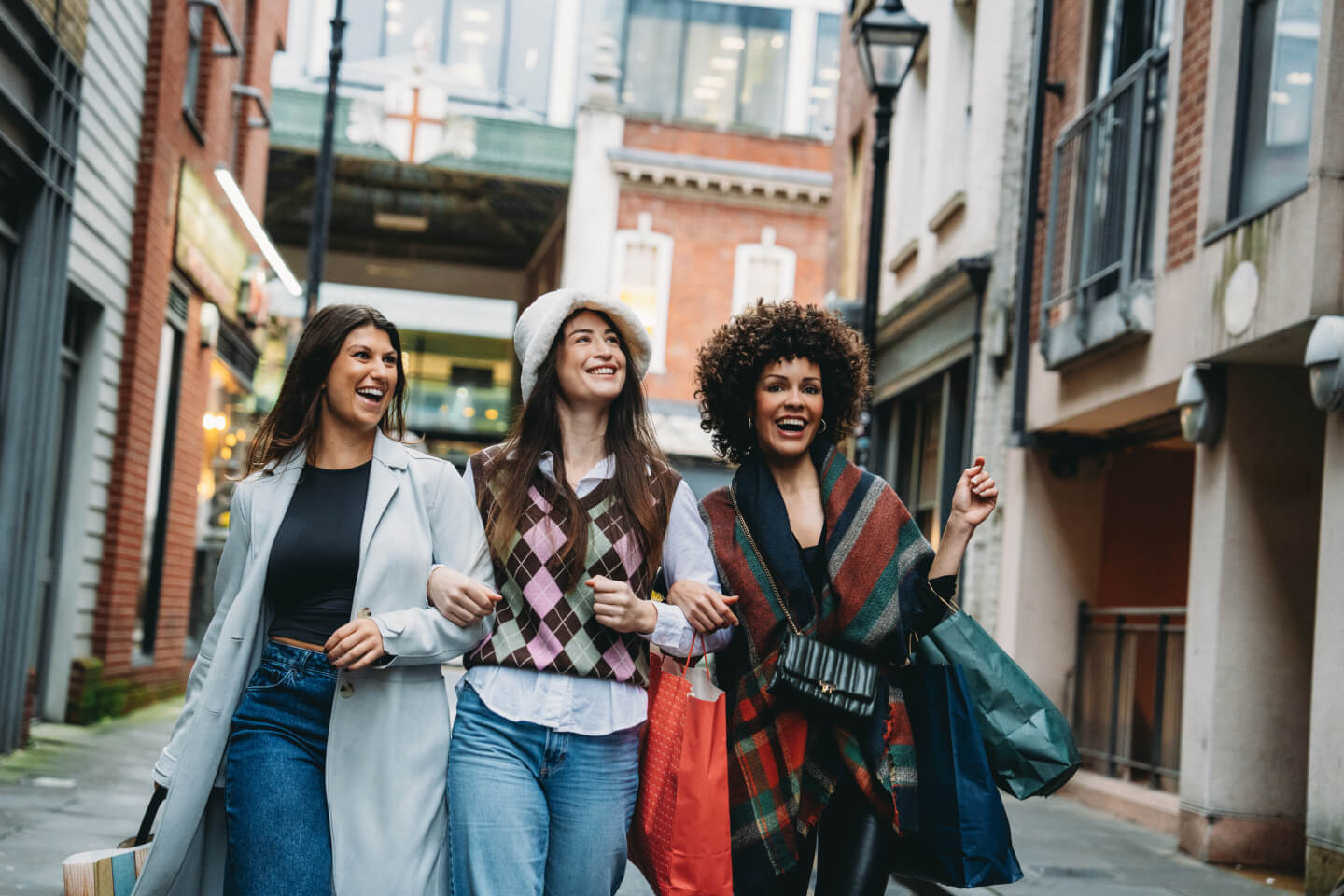 Three young women walking arm-in-arm carrying shopping bags