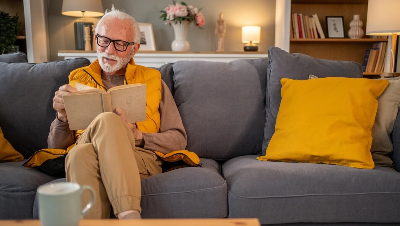 Elder man sat on a sofa reading a book