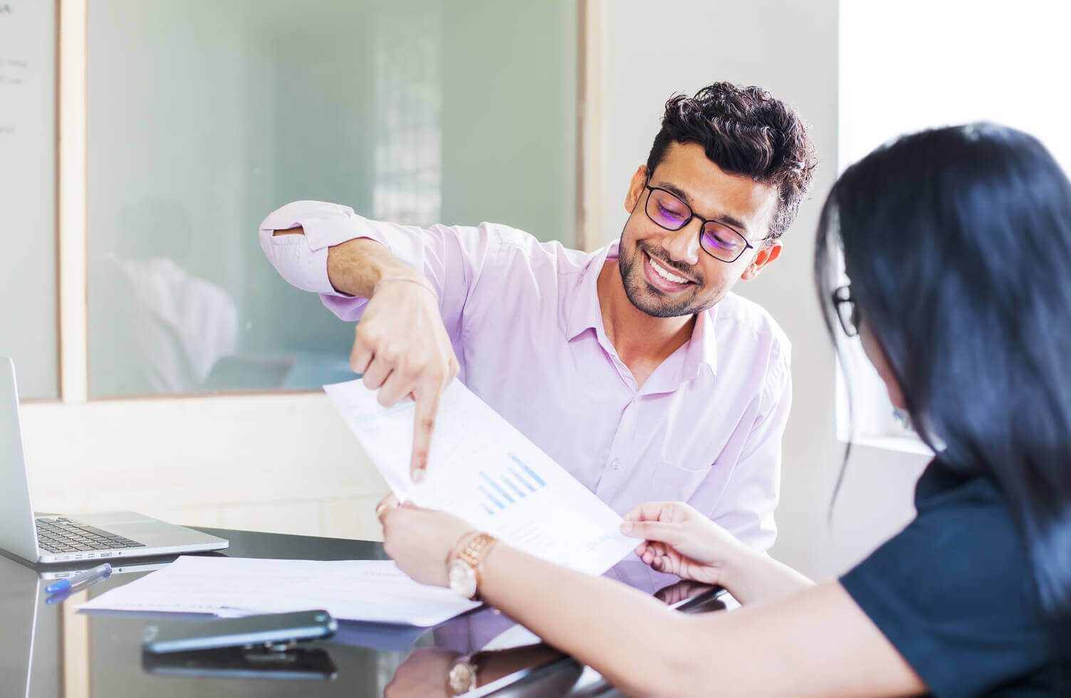 A man and woman looking at a document with a table on it, the man is pointing at the document